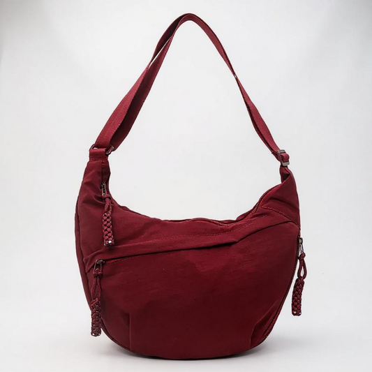 Burgundy crescent-shaped bag with a single adjustable strap and braided zip pulls, shown on a plain light background. 1