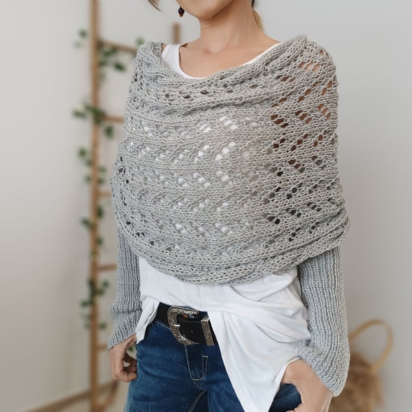Close view of a light grey lace-knit wrap with ribbed sleeves, worn with a white top and belted jeans. 7