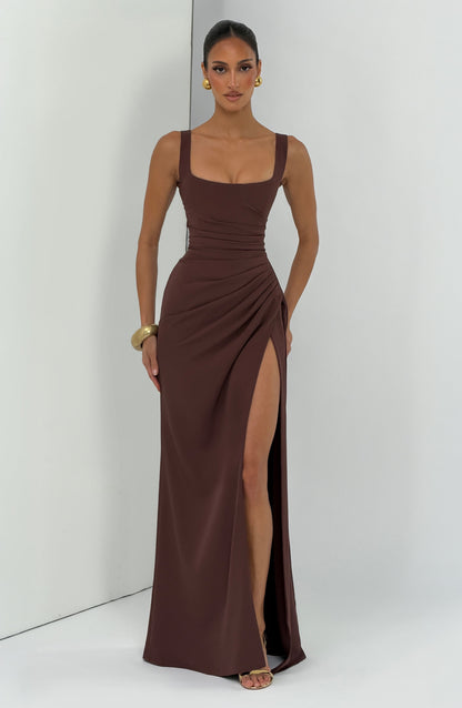 Model in the brown maxi dress standing against a pale panelled studio wall, showing the full-length slit. 8