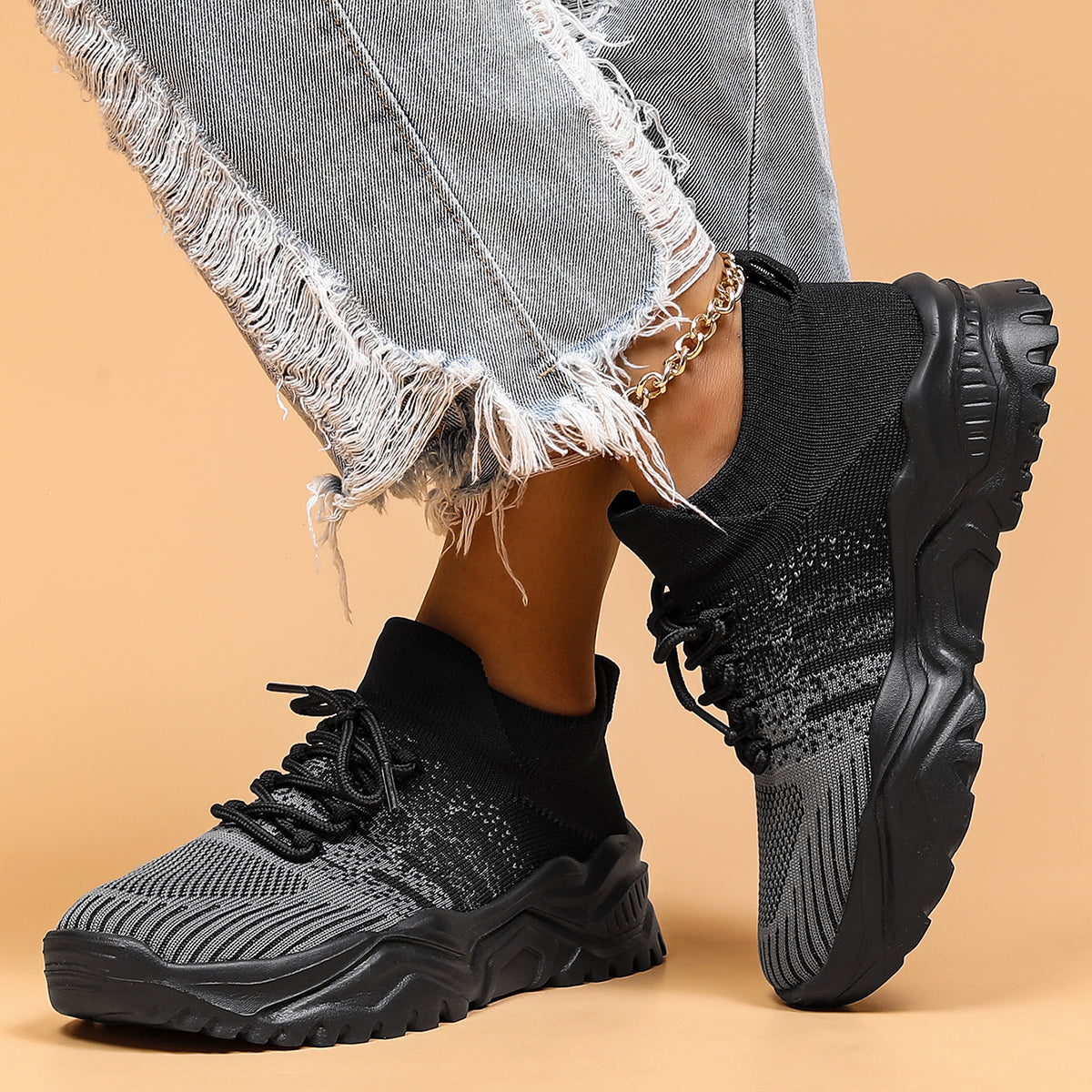 Black and grey knit lace-up sneakers with thick black soles, worn by a model in distressed jeans and a gold anklet. 2