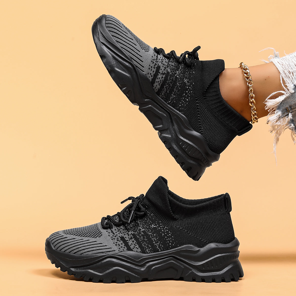 Side view of black and grey gradient knit sneakers with chunky black soles, one shoe raised above the other. 3
