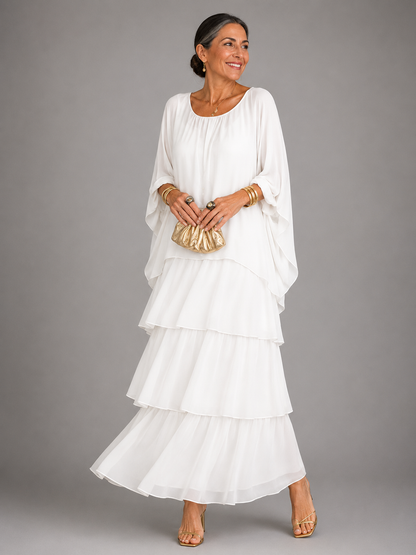 Woman in the white tiered chiffon maxi dress with a gathered neckline and flowing cape sleeves, holding a small gold clutch. 6