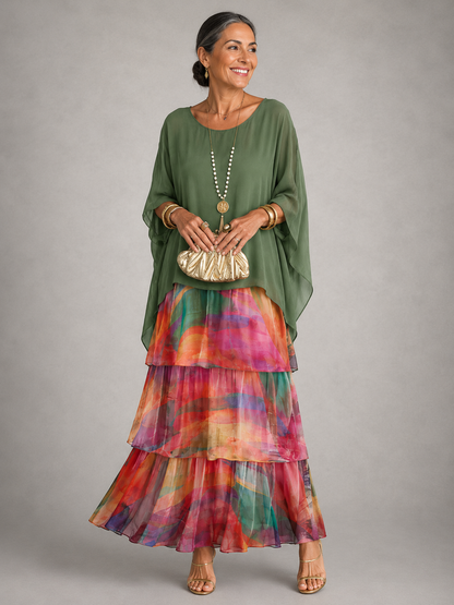 Woman wearing an olive green cape top over a tiered maxi skirt in a colourful watercolour print of pink, orange and teal. 9