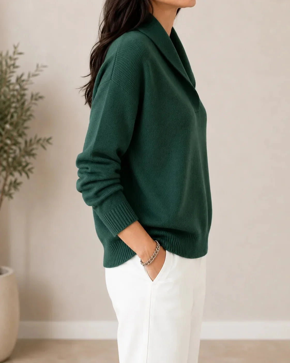 Side view of the dark green jumper on a model, showing the sleeve, ribbed cuff and hem and the collar from the side. 3