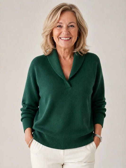 Smiling woman with shoulder-length blonde hair wearing the dark green jumper with white trousers, hands in pockets, against a plain light backdrop. 1