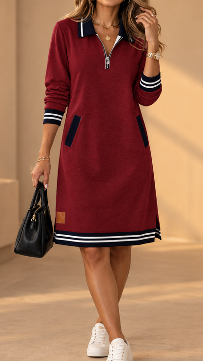 Model wearing the dress in burgundy red with navy and white striped trims, side pockets and small tan patch, paired with white trainers. 3