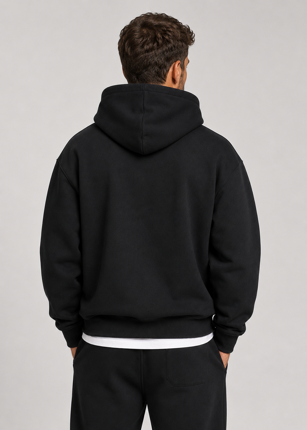 Back view of the black hoodie and joggers on a model, showing the plain back and a patch pocket on the joggers. 5