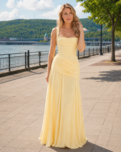 Pale yellow maxi dress worn by a woman with wavy blonde hair on a sunny waterside promenade. 1