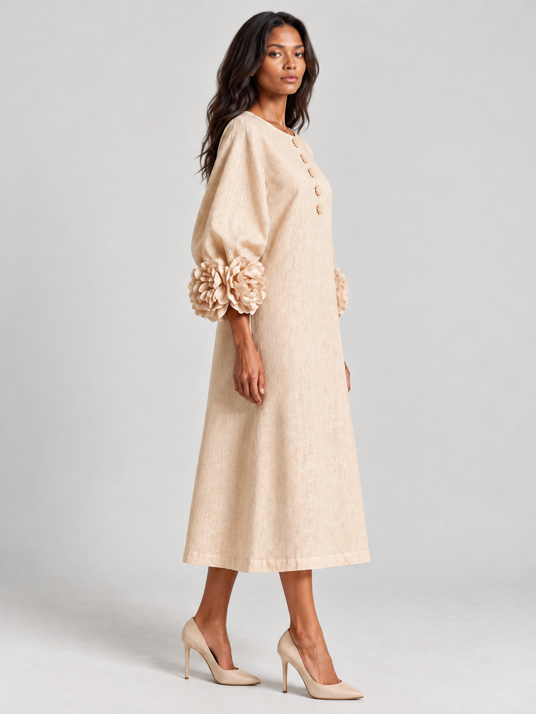 Side view of the beige dress on a model turned to the camera, showing the sleeve volume, floral cuff and A-line skirt. 3