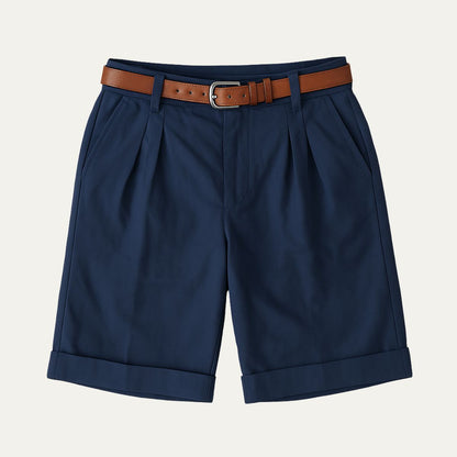 Navy pleated shorts with turn-up hems, laid flat from the front with a tan leather belt and silver buckle. 9
