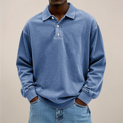 Model wearing the relaxed long sleeve polo in washed mid blue, hands in the pockets of light blue jeans, front view. 1