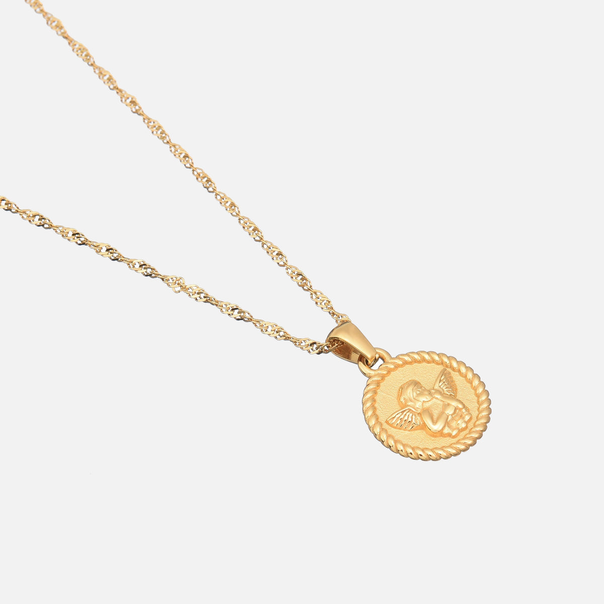Angled view of the round cherub pendant on its twisted gold chain, lying on a pale grey background. 2