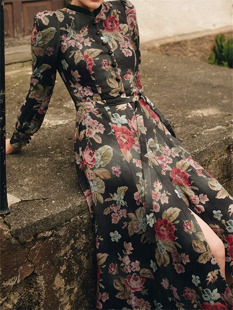 Model seated outdoors on stone steps in the floral dress without the apron, showing the long skirt with a side slit. 3