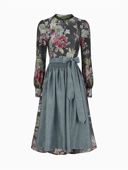 Front view of the dark floral dirndl dress on a plain background, worn with a grey-blue apron tied in a bow. 1