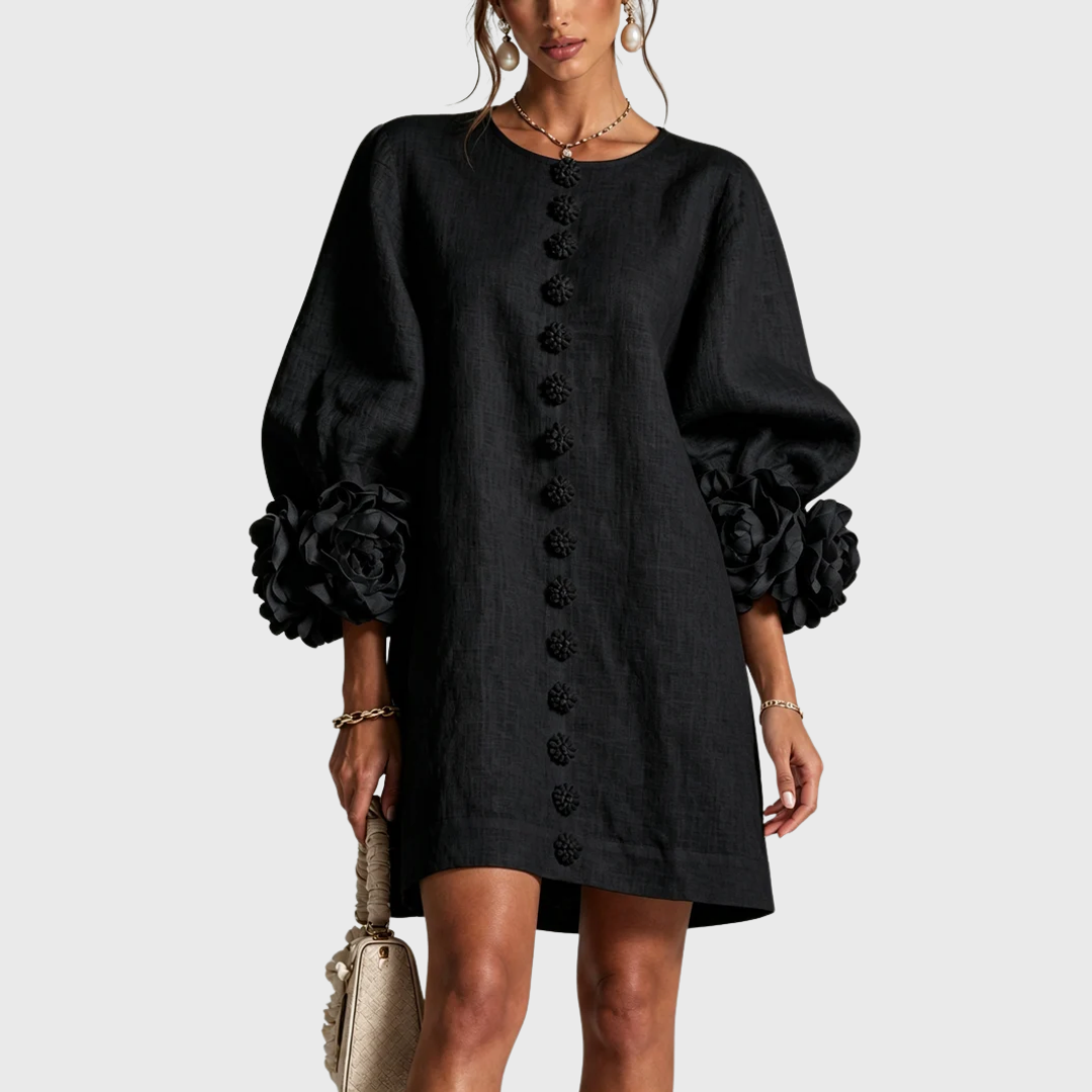 Front view of the dress in black on a model, showing the textured fabric, flower buttons and rosette cuffs. 4