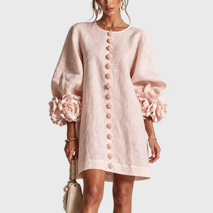 Front view of the dress in soft blush pink on a model, with tonal flower buttons and cuff rosettes. 5