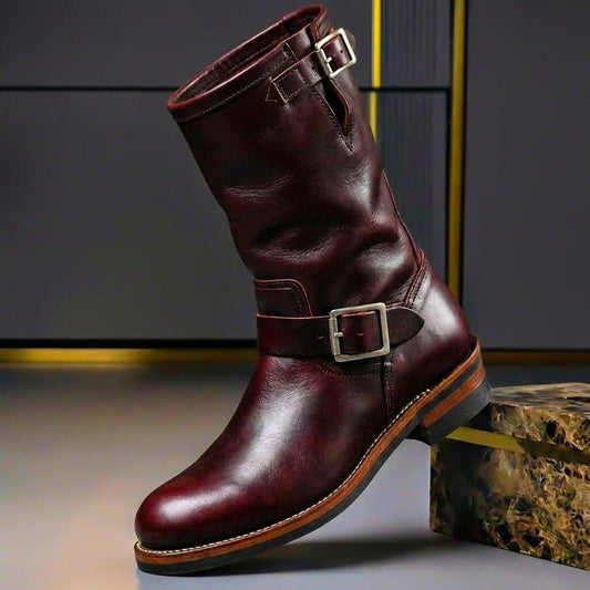 Dark burgundy leather engineer boot with silver-toned buckles and a stitched welt sole, posed beside a marble-effect block. 2