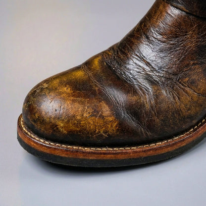 Close-up of the rounded toe of a worn brown leather boot, showing creasing, scuffs and the stitched welt. 6