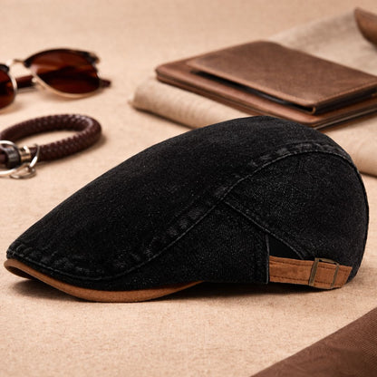 Black denim version of the flat cap with tan peak and buckle strap, shown beside sunglasses, a bracelet and a wallet. 8