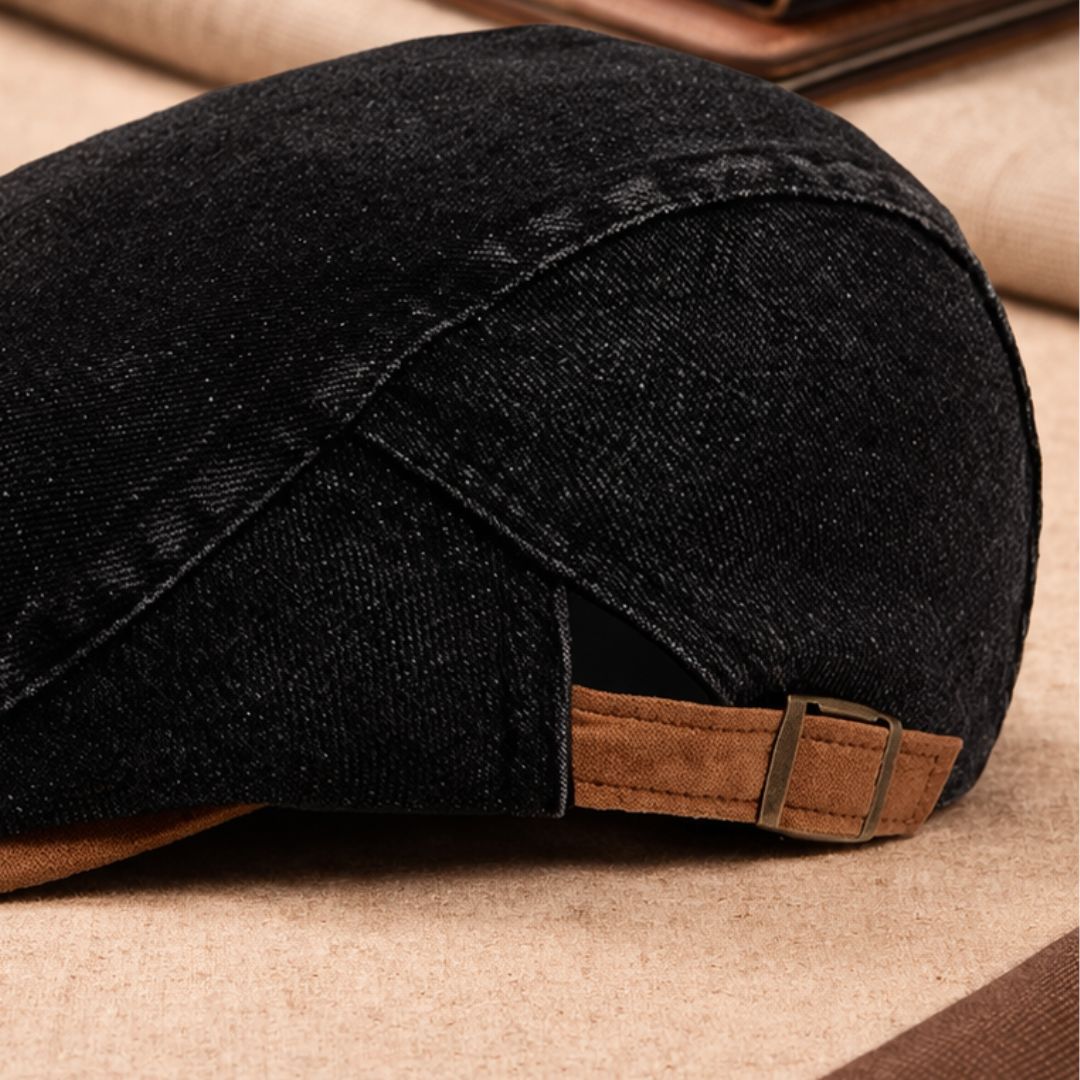 Close-up of the black denim cap's rear, showing the seam detail and tan strap with brass-coloured adjustment buckle. 9