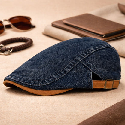 Dark navy denim version of the flat cap with tan peak and buckle, styled among accessories on a beige surface. 7