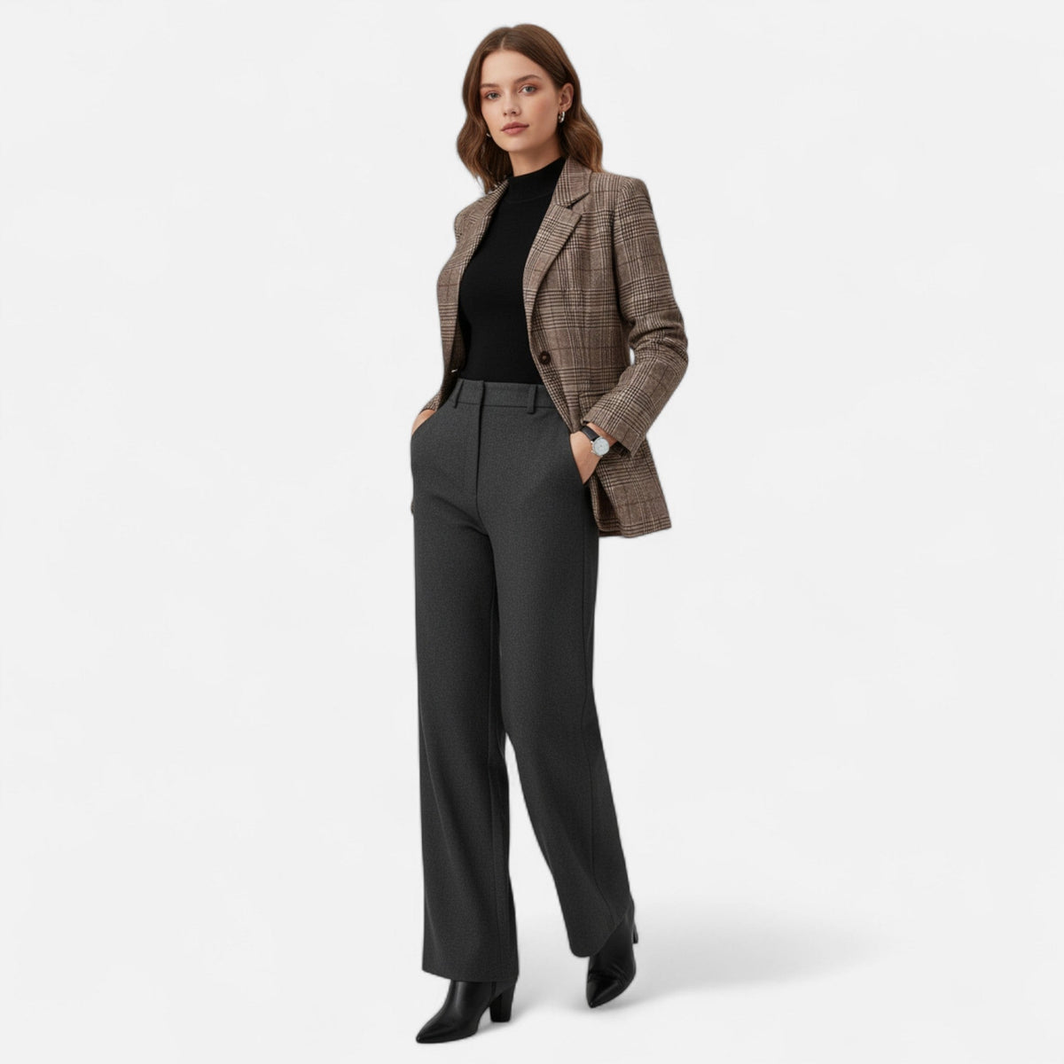 Full-length front view of a model wearing the brown checked blazer with a black top, grey tailored trousers and black ankle boots, hands in pockets. 2