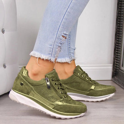Model wearing the olive-green version of the trainers, showing the side zip, metallic trim and studded panel on a white sole. 4