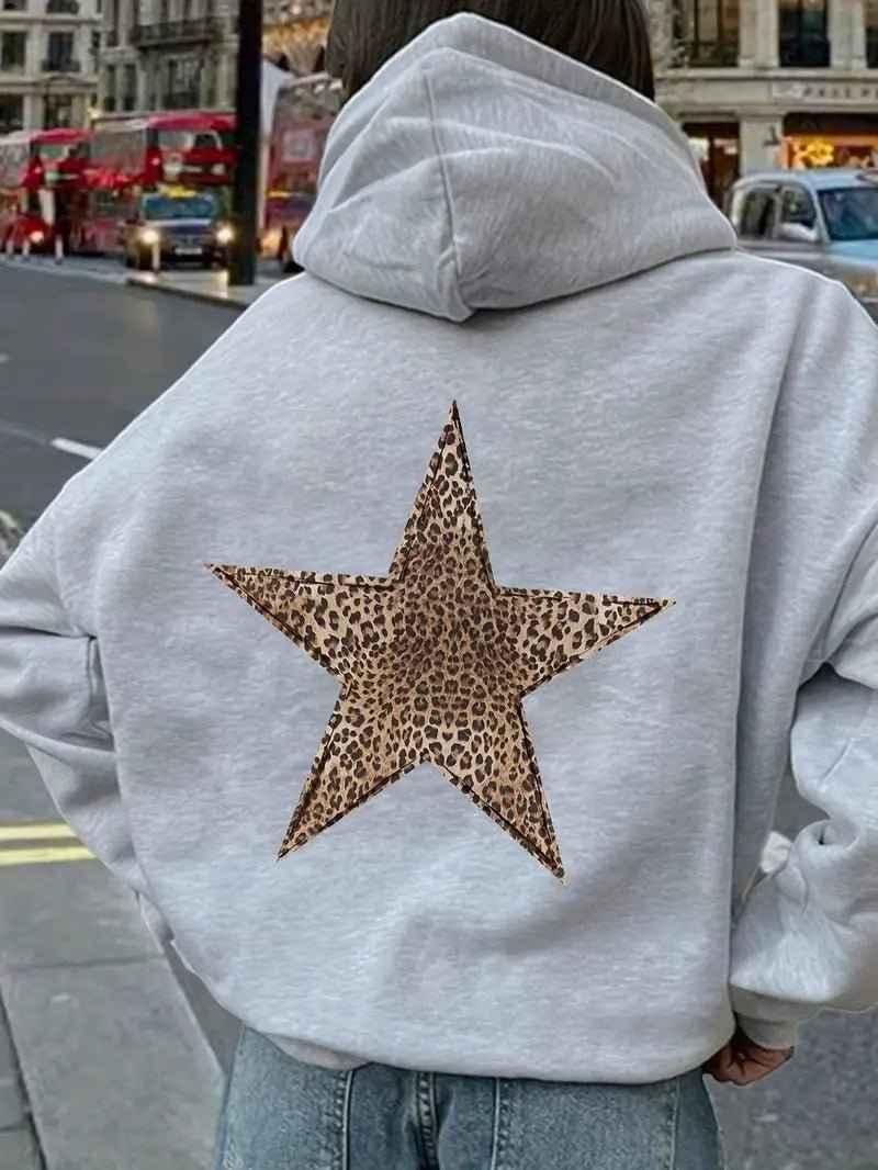 Close back view of a model in the light grey hoodie, the big leopard-print star centred, with a London street behind. 3