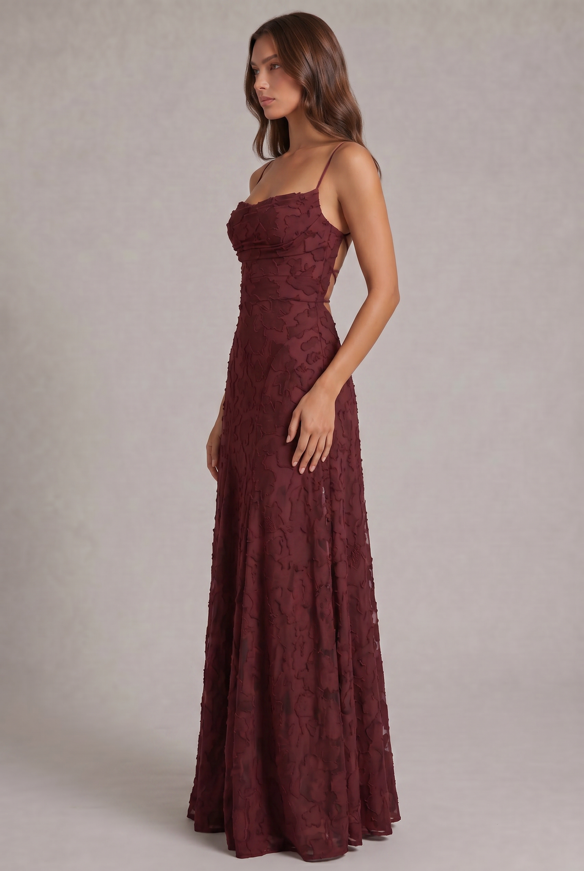 Side view of the burgundy maxi dress on a model, showing the fitted bodice, draped neckline and flowing skirt. 4
