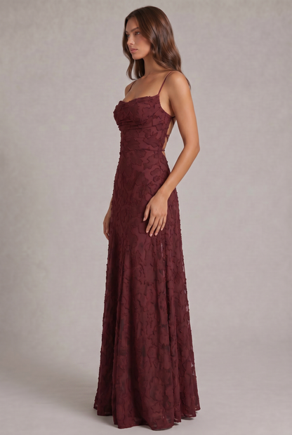 Side view of the burgundy maxi dress on a model, showing the fitted bodice, draped neckline and flowing skirt. 4