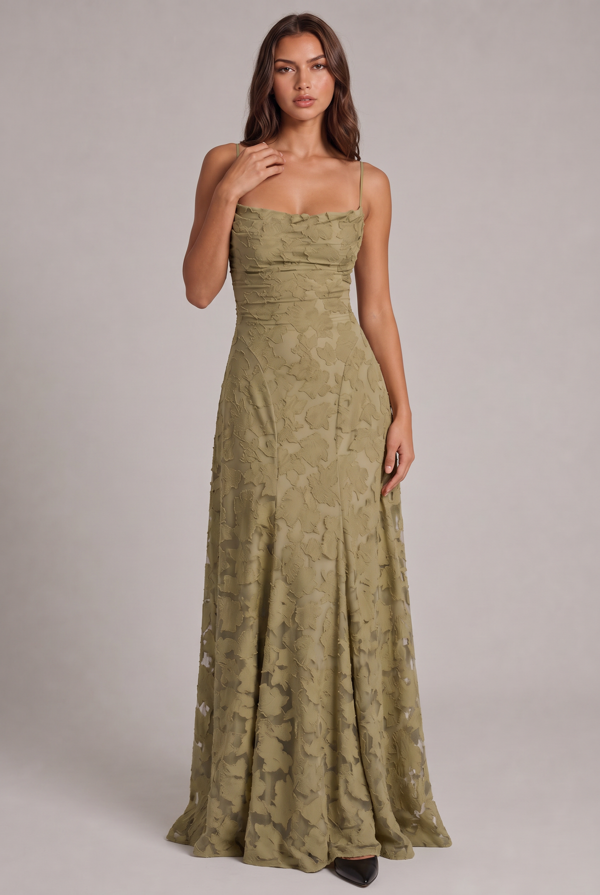 Model wearing the olive green floral-textured maxi dress with thin straps, full-length front view with one hand at her collarbone. 13
