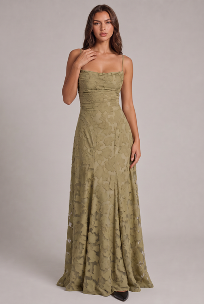 Model wearing the olive green floral-textured maxi dress with thin straps, full-length front view with one hand at her collarbone. 13