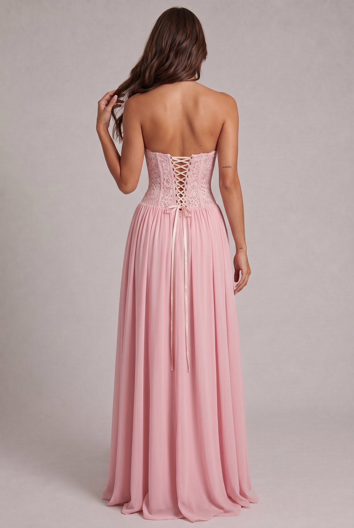 Back view of the pink dress on a model, showing the open back, lace-up corset and long satin ribbon ties. 4