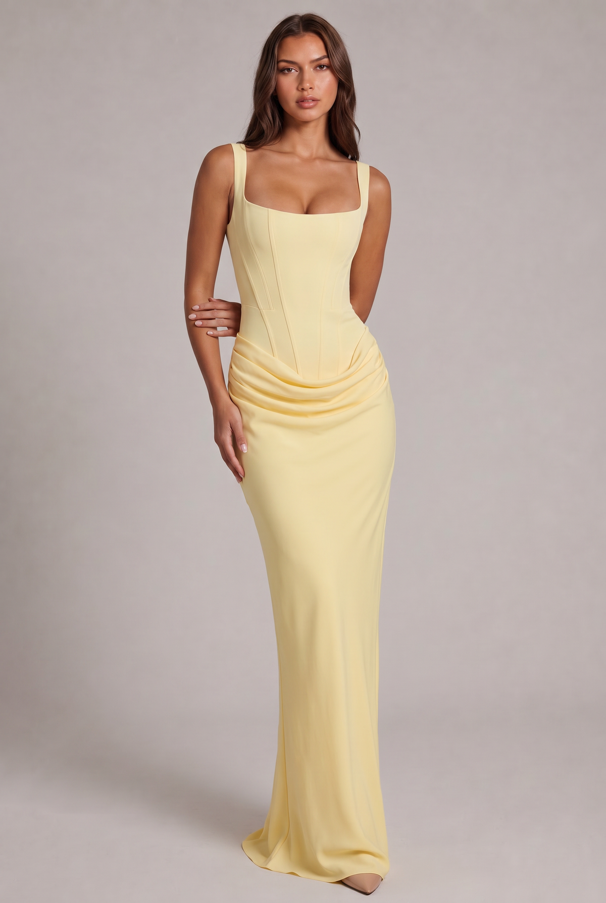 Model standing full-length in the pale yellow maxi dress, showing the boned corset bodice, square neckline and draped hip detail. 21