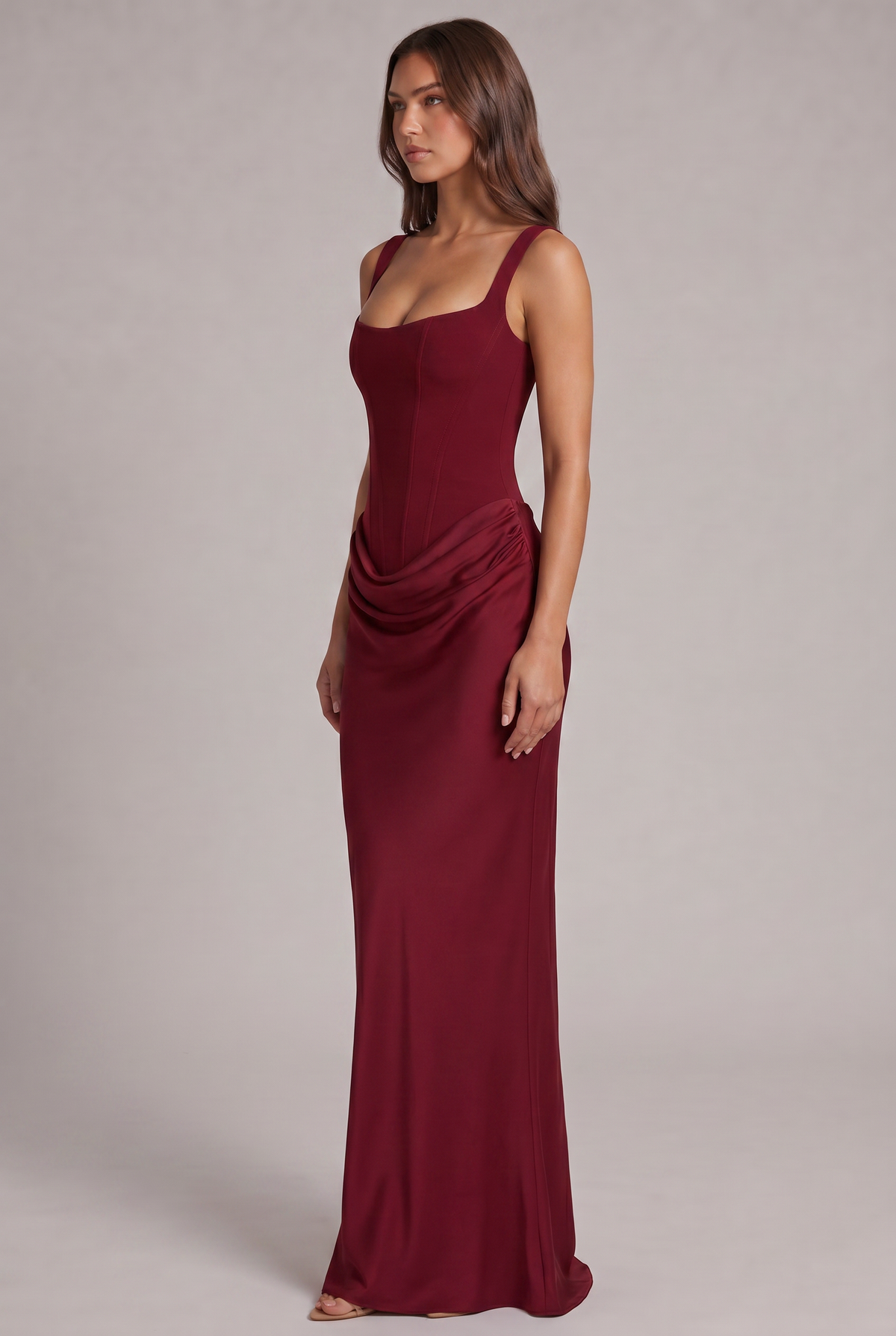 Side view of the burgundy maxi dress, showing the structured corset bodice, draped hip detail and long fitted skirt. 19