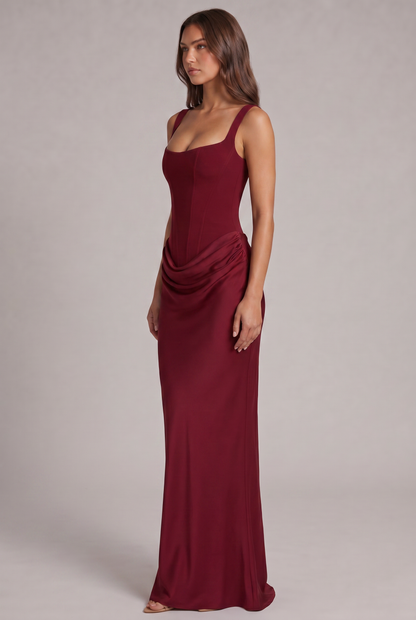 Side view of the burgundy maxi dress, showing the structured corset bodice, draped hip detail and long fitted skirt. 19