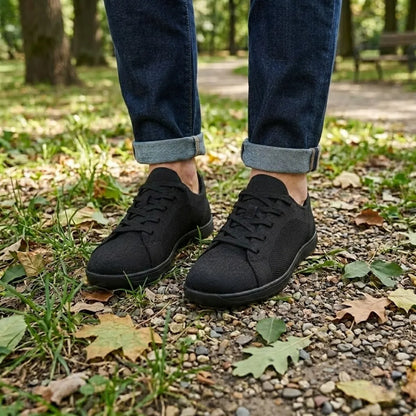 Pair of black knit trainers worn with rolled dark jeans, standing on gravel and fallen leaves in a park. 11