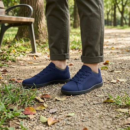 Pair of navy knit trainers with black soles worn with rolled olive trousers, standing on a gravel park path. 20
