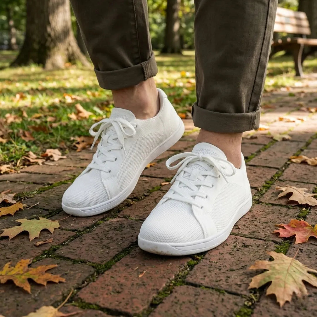 Person wearing white knit trainers with olive trousers rolled at the ankle, walking on brick paving among autumn leaves. 38