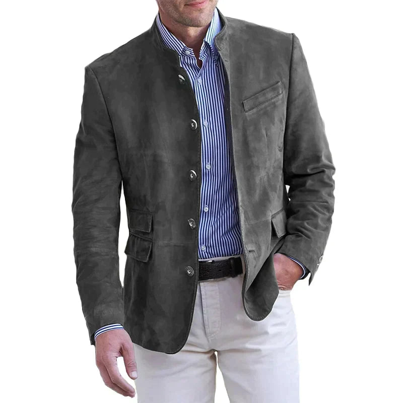 Man wearing the stand-collar button-front jacket in dark grey over a blue striped shirt and cream trousers, hand in pocket. 2