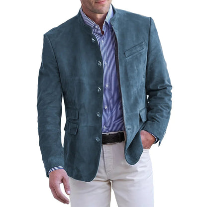 Man wearing the stand-collar jacket in teal blue suede-look fabric over a striped shirt and cream trousers, one hand in pocket. 1