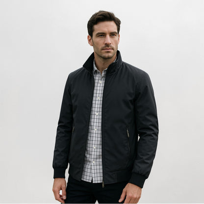 Model wearing the jacket in black, open over a checked shirt and dark trousers, showing the stand collar and zipped pockets. 2