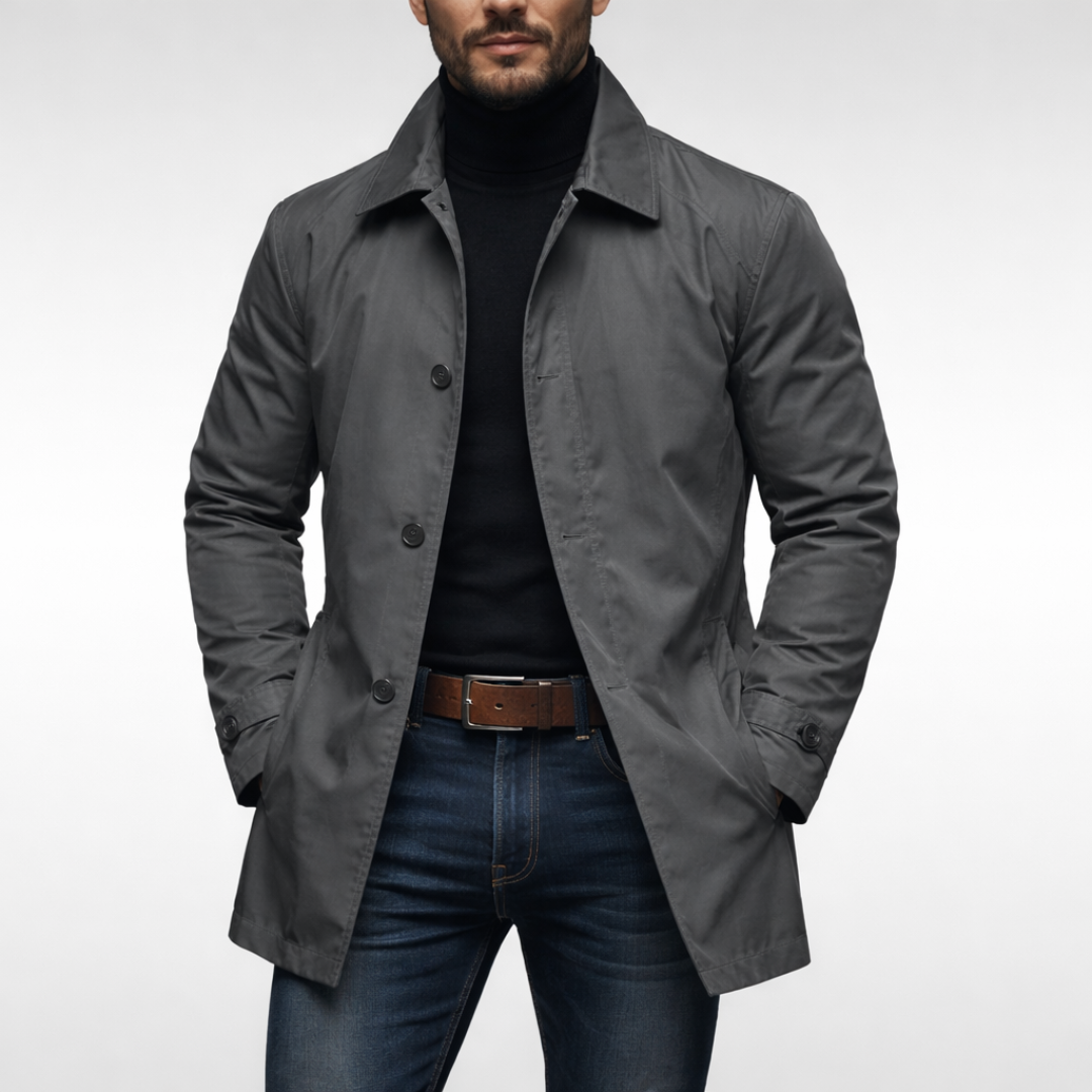 Front view of the grey button-front jacket worn open over a black roll-neck, jeans and brown leather belt, studio backdrop. 1