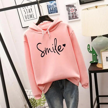 Pink version of the hooded sweatshirt with the same black script slogan and heart, hanging on a hanger over blue jeans. 2