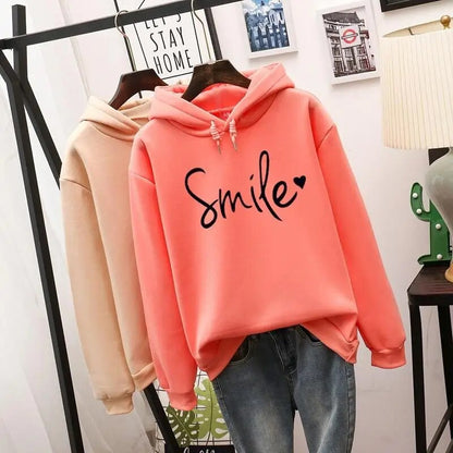 Coral-orange hoodie with black script slogan in front, with the beige hoodie hanging behind it on the same rail. 3