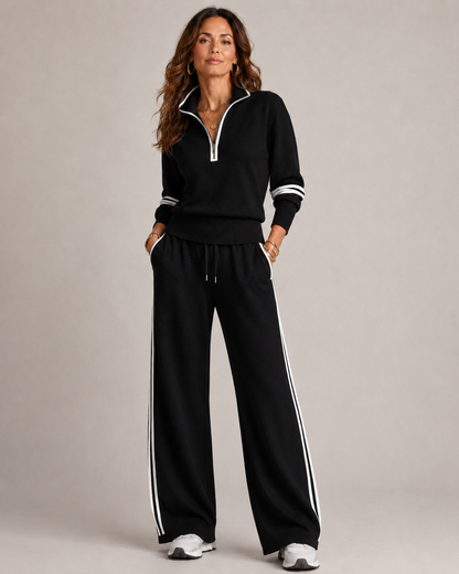 Model standing in the black set with white piping and side stripes, hands in pockets, finished with white trainers. 5