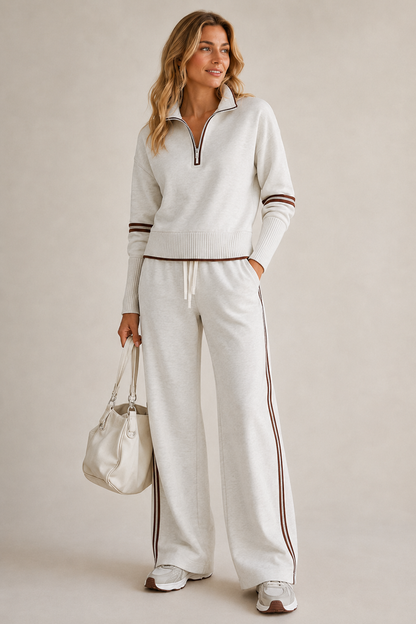 Model in the light grey marl set with brown stripes, one hand in pocket, holding a cream handbag and wearing trainers. 1