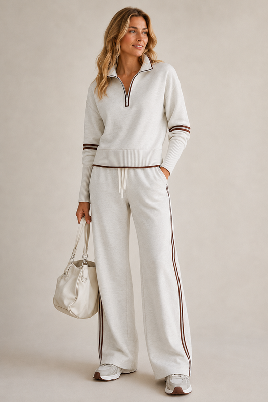 Model in the light grey marl set with brown stripes, one hand in pocket, holding a cream handbag and wearing trainers. 1