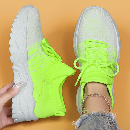Top-down view of neon yellow-green knit sneakers fading to white, with chunky white soles, one held in hand and one worn with a gold ankle chain. 21