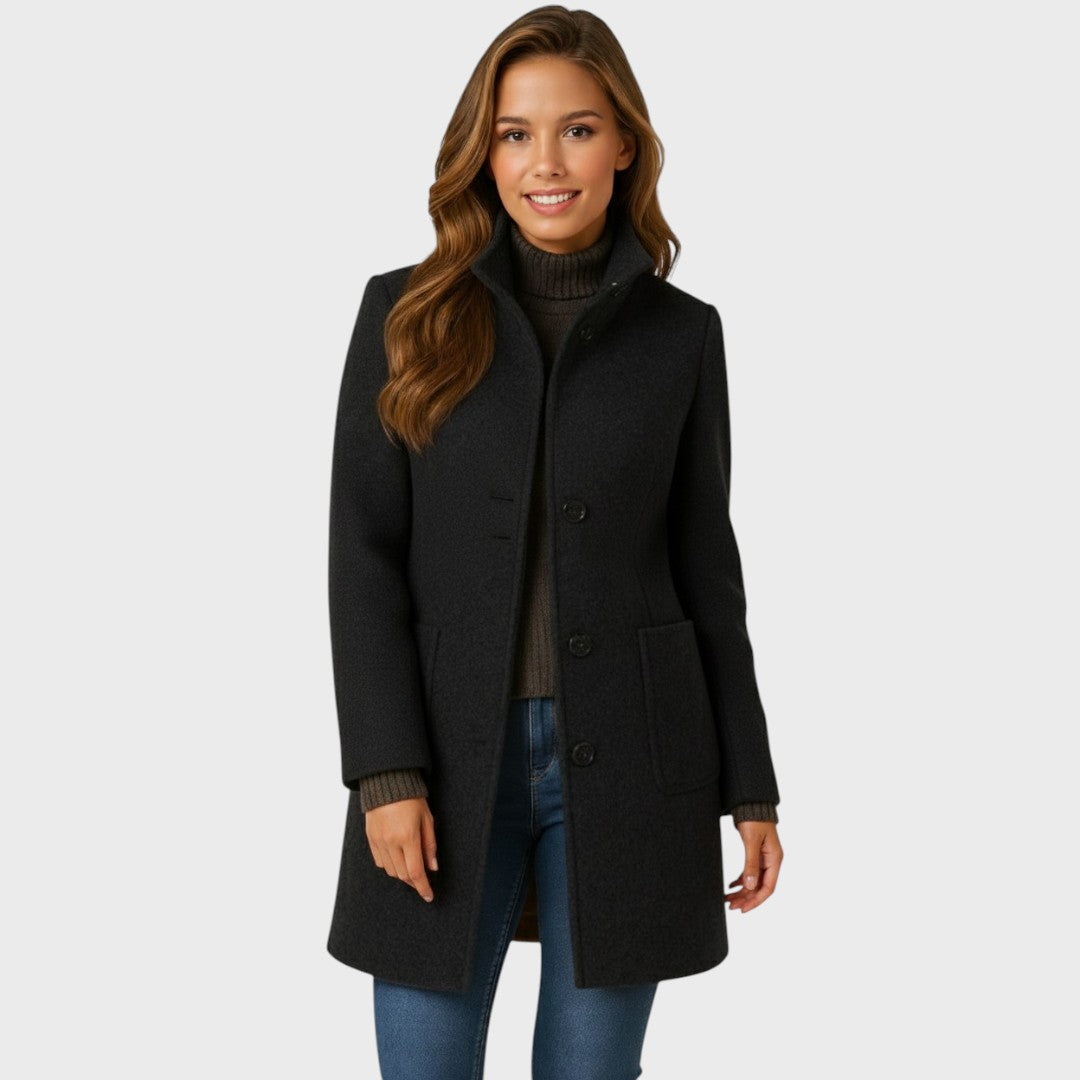 Smiling model wearing the black version of the coat, left open over a brown roll-neck jumper and blue jeans. 3